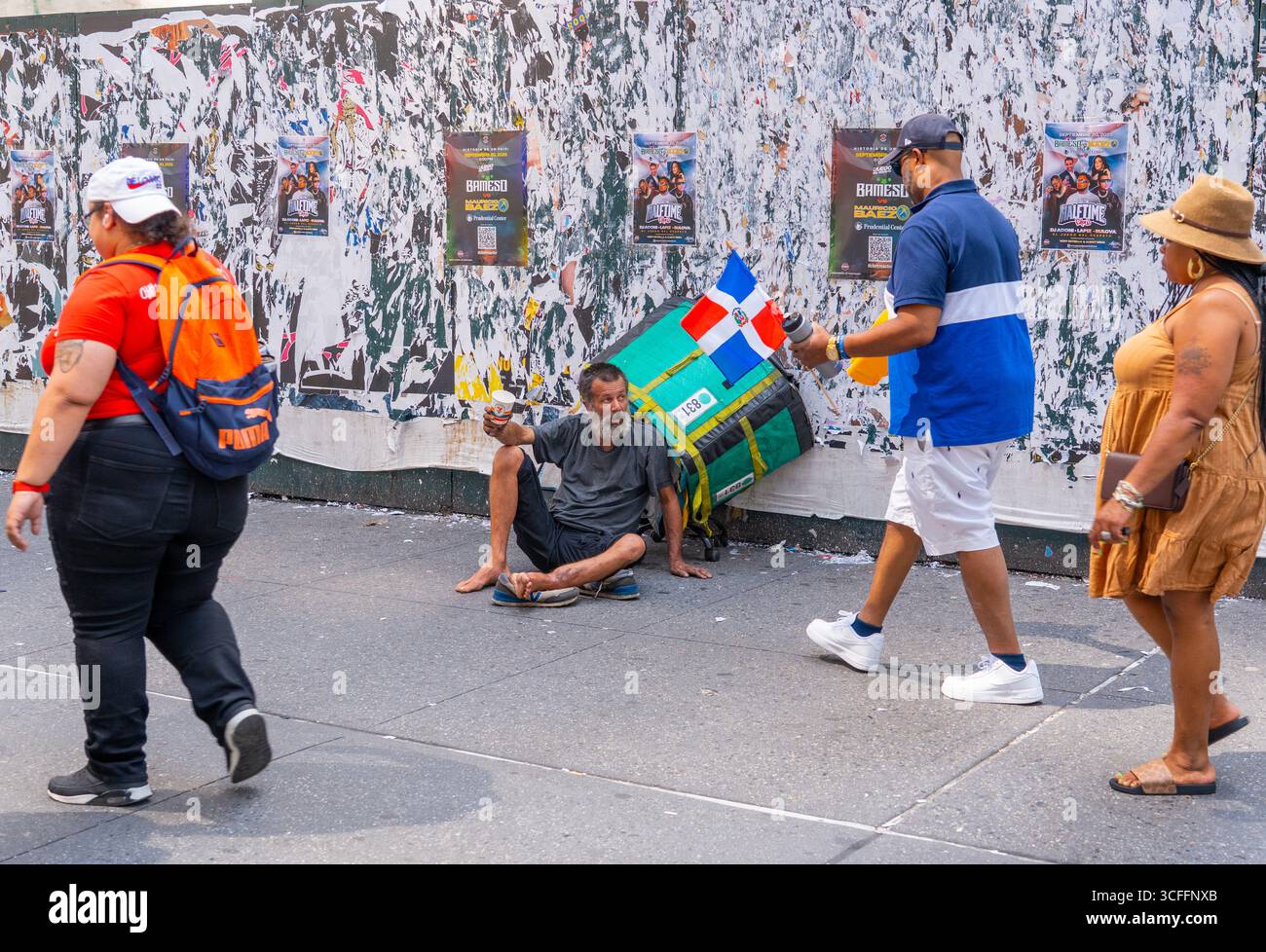Le persone che partecipano alla National Dominican Day Parade passano accanto a un senzatetto che chiede aiuto lungo la 6th Avenue a New York City. Foto Stock