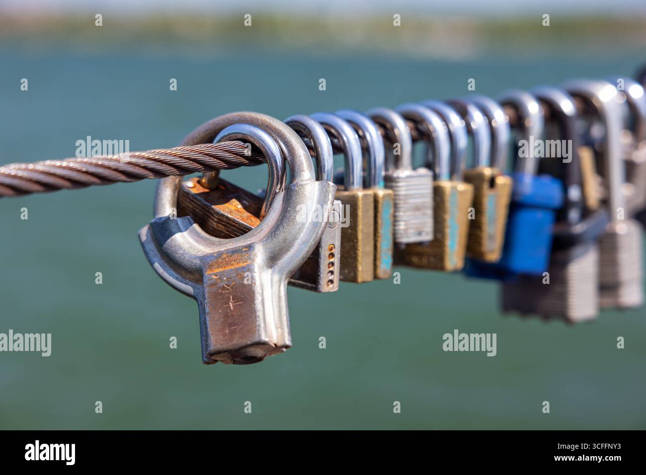 Una fila di Padlocks of Love su un cavo d'acciaio vicino all'acqua. Foto Stock