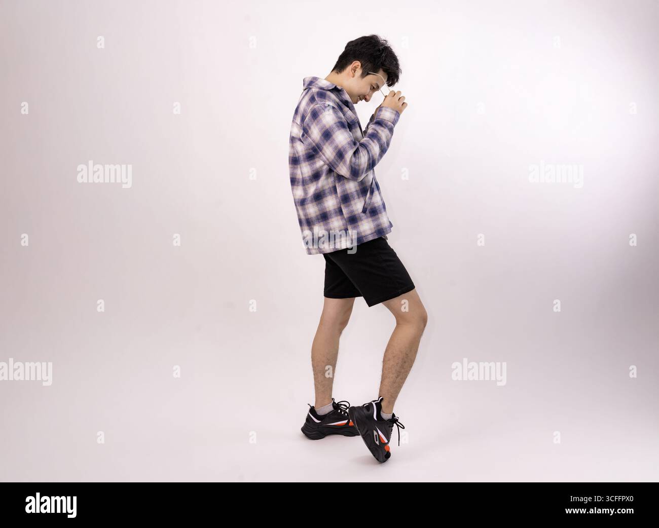 giovane uomo che regola gli occhiali in un ambiente casual con ritratti in studio Foto Stock