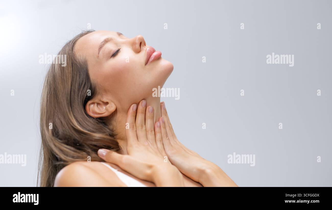 La donna con una pelle sana tocca dolcemente il collo, trasudando tranquillità e sicurezza, circondata da una luce rilassante che esalta il suo beau naturale Foto Stock
