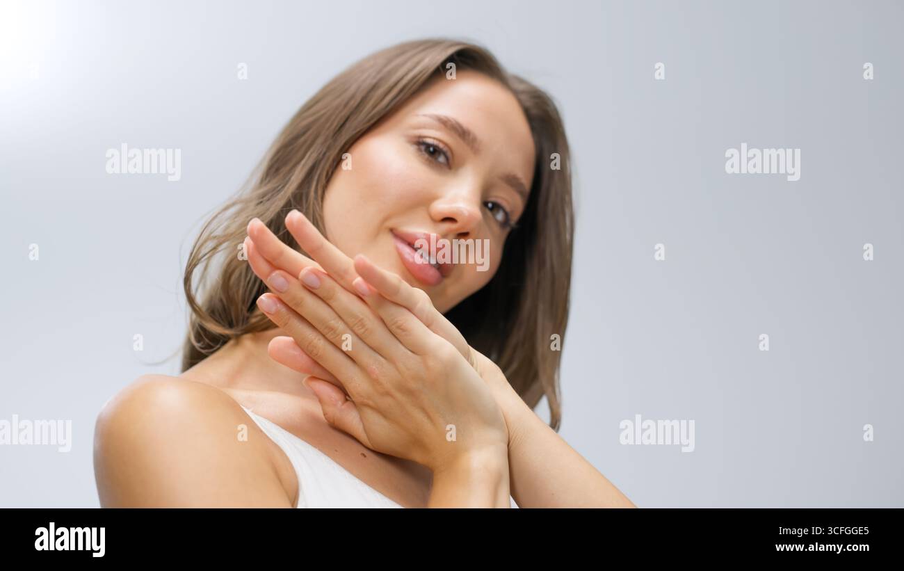 La donna con la pelle luccicante tocca dolcemente il viso, evidenziando la sua colorazione radiosa in un ambiente tranquillo, rappresentando temi di benessere e cura della pelle Foto Stock