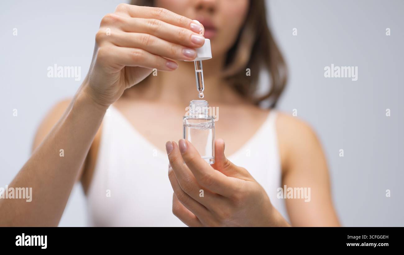 La modella femminile tiene in mano un flacone contagocce di siero per la cura della pelle, sottolineando la sua sana routine di benessere, circondata da un'atmosfera serena che Foto Stock