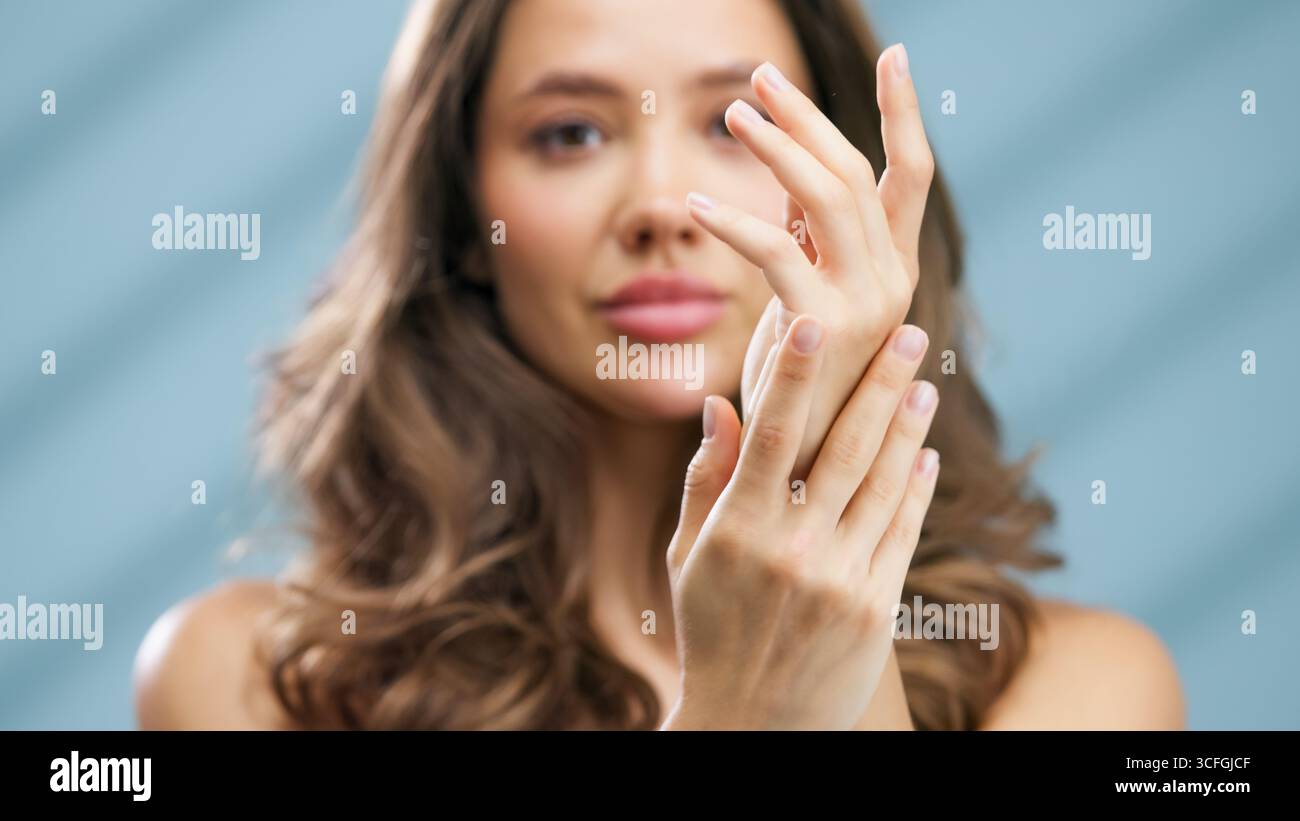 Giovane donna con lunghi capelli castani sta applicando idratante alle sue mani, evidenziando la bellezza della pelle sana e il significato della routine della cura della pelle Foto Stock