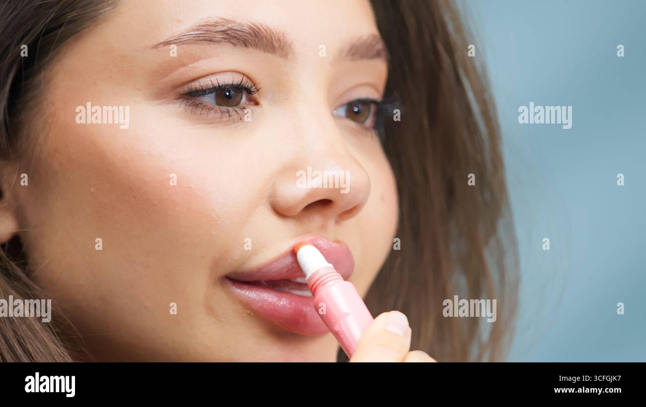 Primo piano di una giovane donna che utilizza un applicatore di balsamo rosa per labbra, evidenziando la sua pelle sana e la sua bellezza naturale. La scena cattura l'essenza della pelle Foto Stock