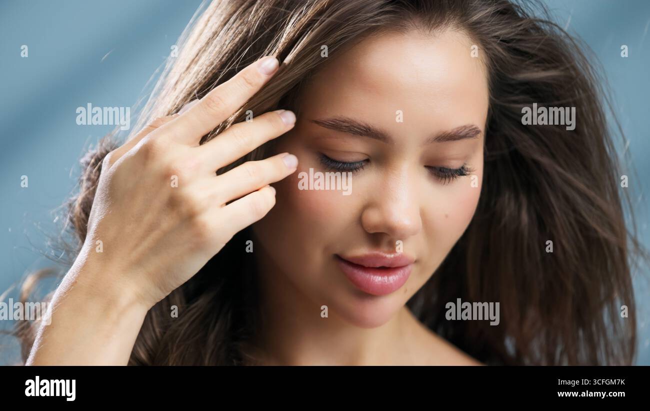 Una giovane donna con una pelle radiosa tocca delicatamente i suoi capelli, evidenziando la sua bellezza naturale. La scena è inondata di luce delicata, creando un invito Foto Stock