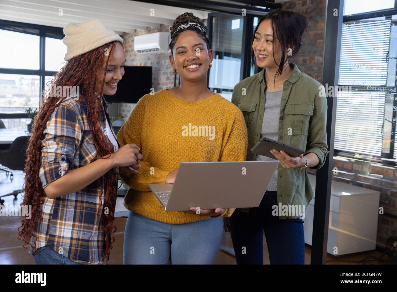 Diverse colleghe che collaborano con notebook e tablet in un moderno spazio open space per uffici Foto Stock