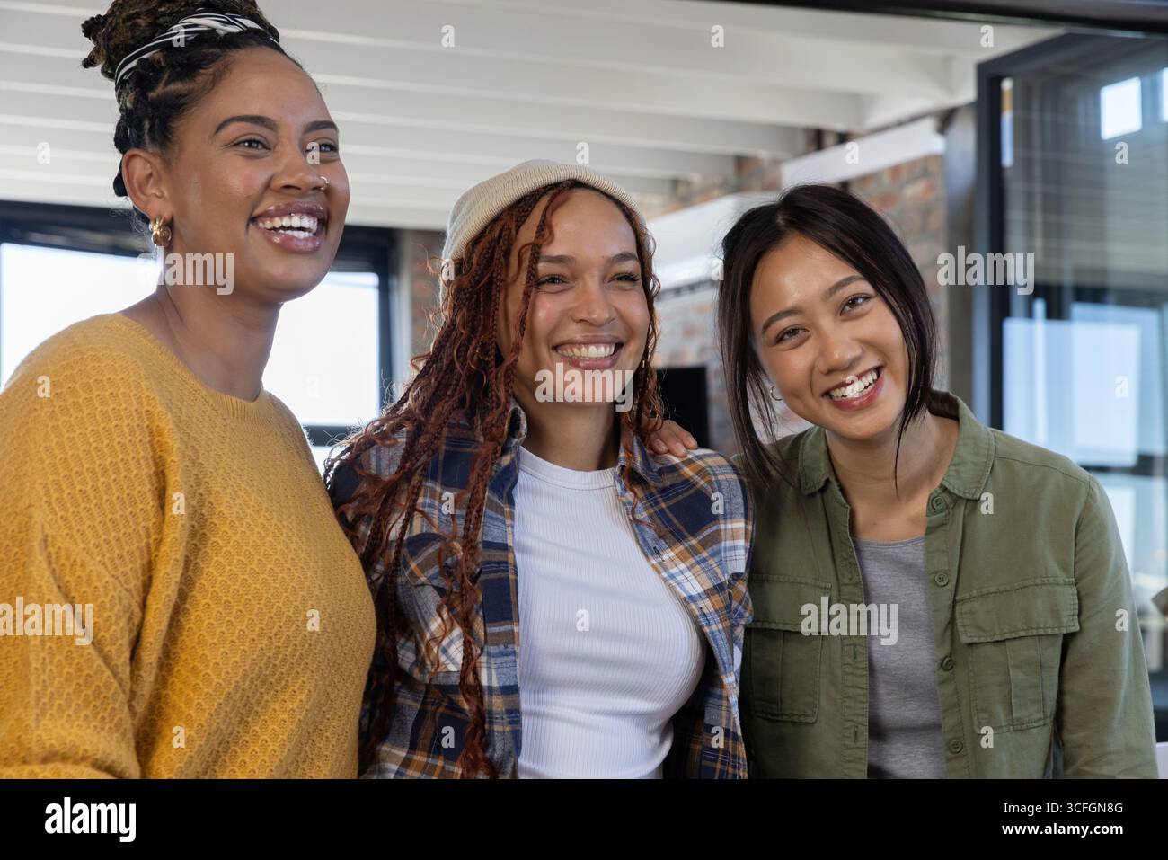 Diverse collaboratrici che si pongono a braccio in un ufficio moderno con mattoni a vista e pareti divisorie in vetro Foto Stock