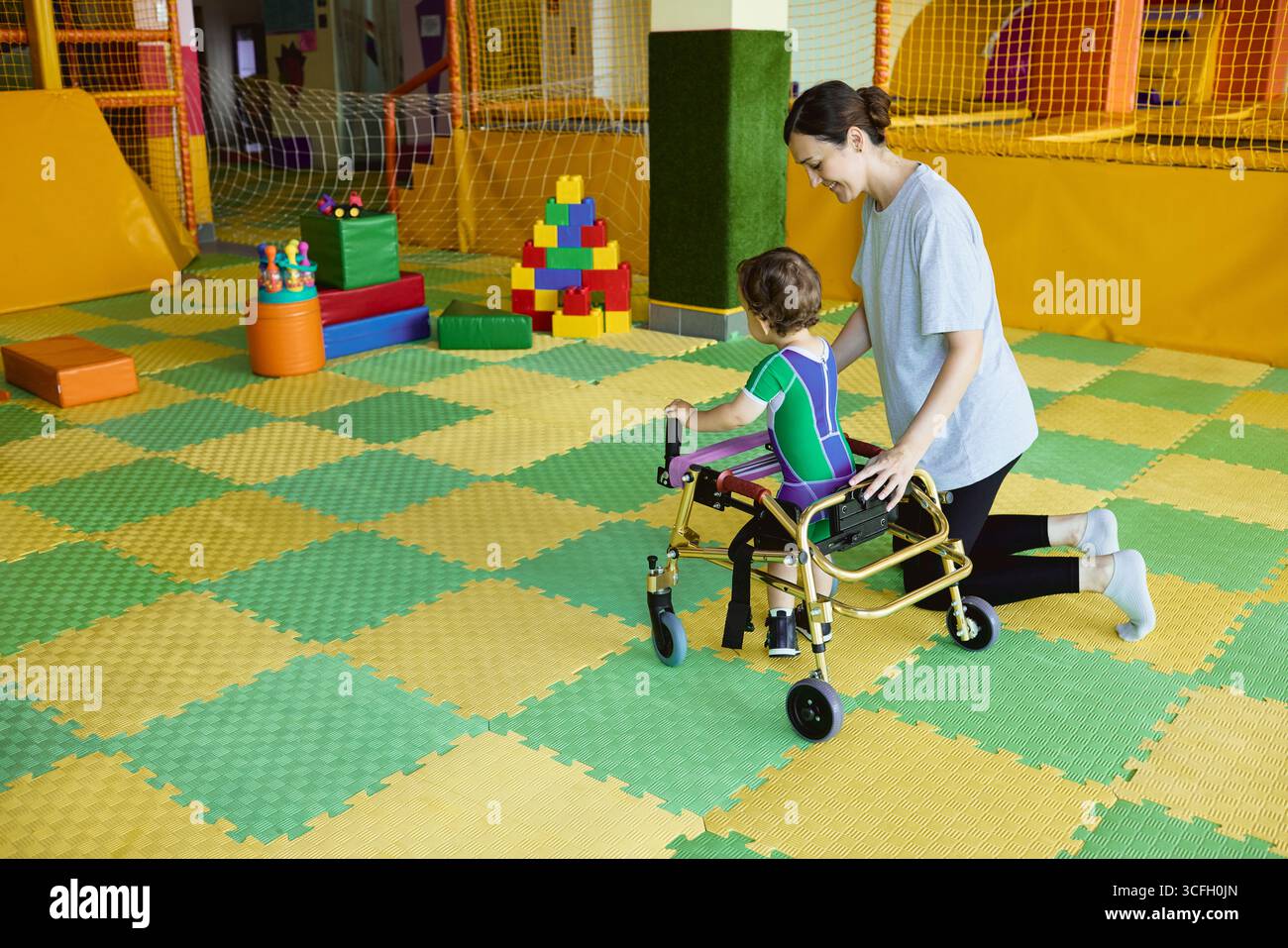 Il fisioterapista assiste il bambino con disturbi muscolo-scheletrici utilizzando ausili alla mobilità durante gli esercizi di riabilitazione in un ambiente di supporto Foto Stock
