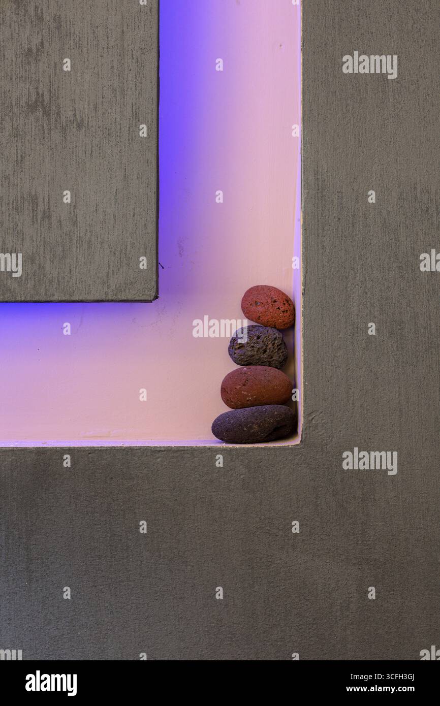 Una disposizione verticale di pietre vulcaniche collocate in modo ordinato nell'angolo di una moderna struttura architettonica. L'illuminazione rosa-viola tenue e la rete lin pulita Foto Stock