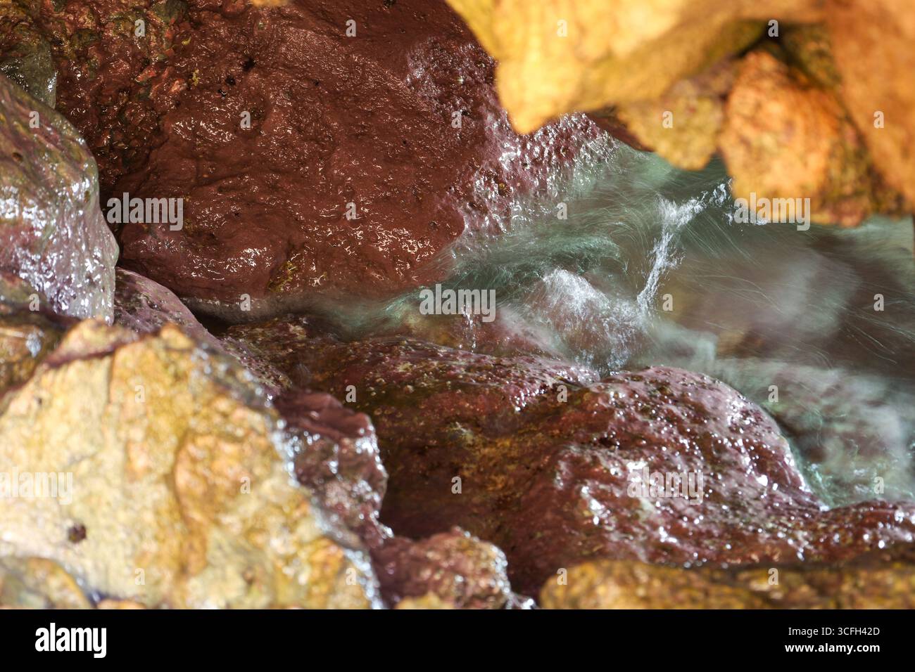 Vista ravvicinata di rocce colorate bagnate con acqua di mare che scorre all'interno di una grotta marina. La texture naturale, la sfocatura del movimento e l'illuminazione creano un organo astratto Foto Stock