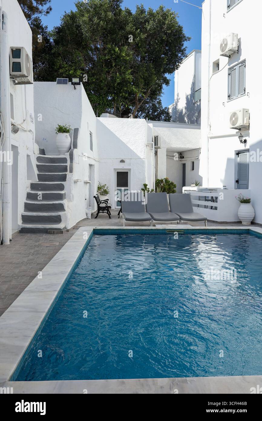 Tranquillo scenario di una piccola piscina privata circondata dalla tradizionale architettura bianca delle Cicladi. Sedie a sdraio, piante in vaso e scale curve evocano un rel Foto Stock