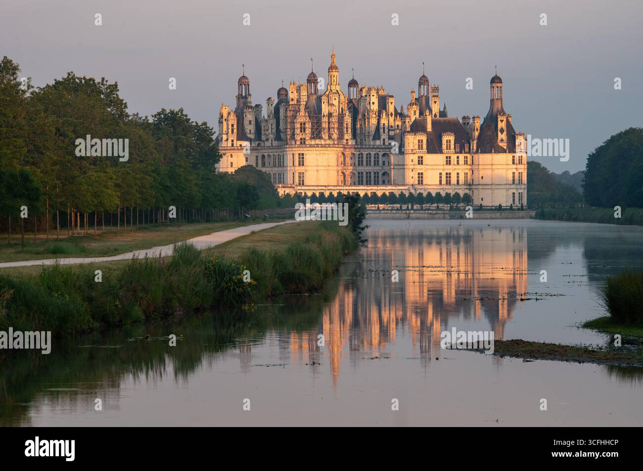 Vista media del Castello di Chambord nella Valle della Loira riflessa nell'acqua durante la luce mattutina dell'ora d'oro Foto Stock