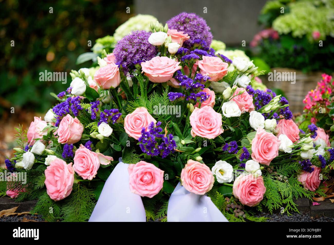 Un bellissimo e dettagliato primo piano di una corona funeraria, caratterizzato da un elegante mix di rose rosa, vivace allium viola e delicati fiori bianchi Foto Stock