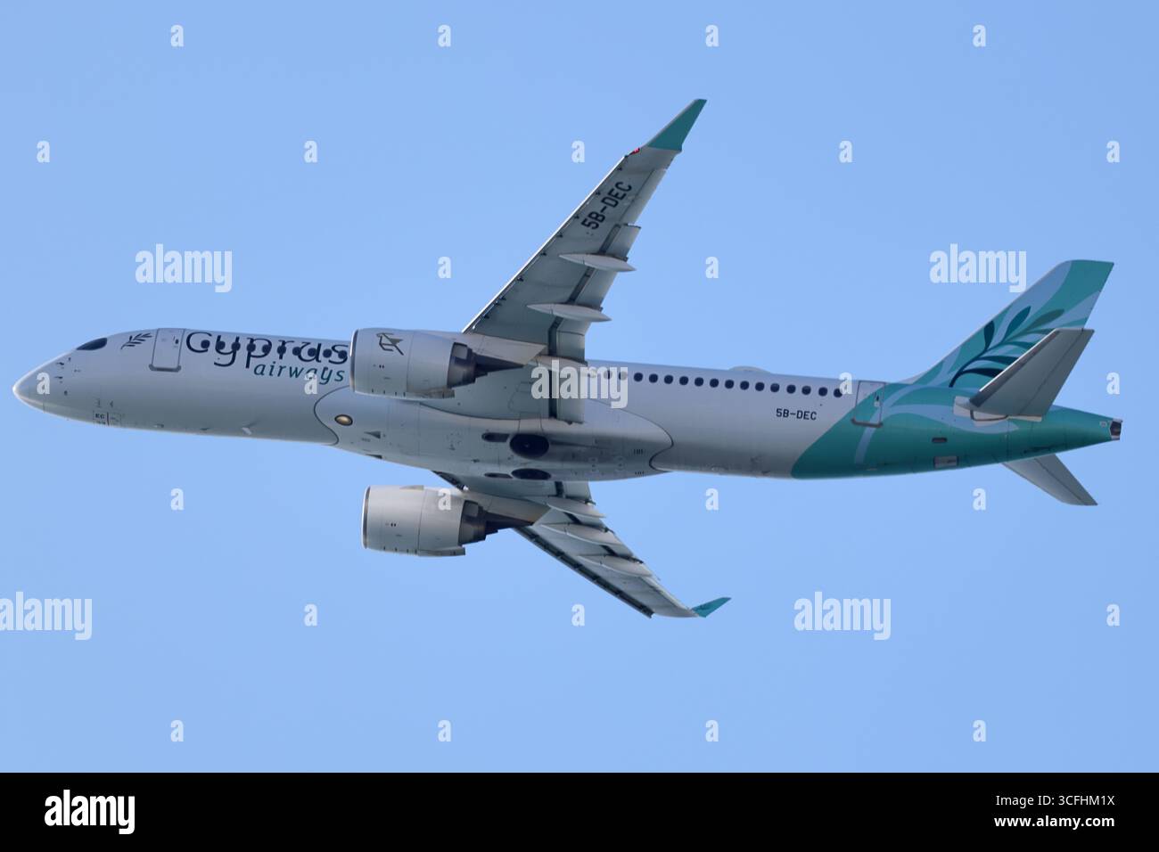 Airbus A220-300 5B-DEC di Cyprus Airways in volo sopra l'aeroporto internazionale di Larnaka, Cipro, mostrando la parte inferiore e le alette contro un cielo limpido. Foto Stock