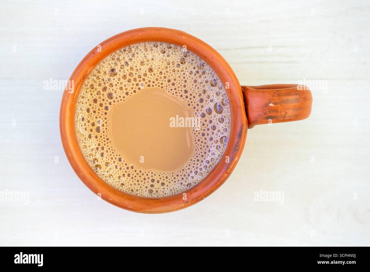 Una tazza di tè al latte caldo o di dudh cha in una tradizionale tazza di argilla. Vista dall'alto del doodh chai in una tazza di terracotta su una superficie di legno chiaro. Foto Stock