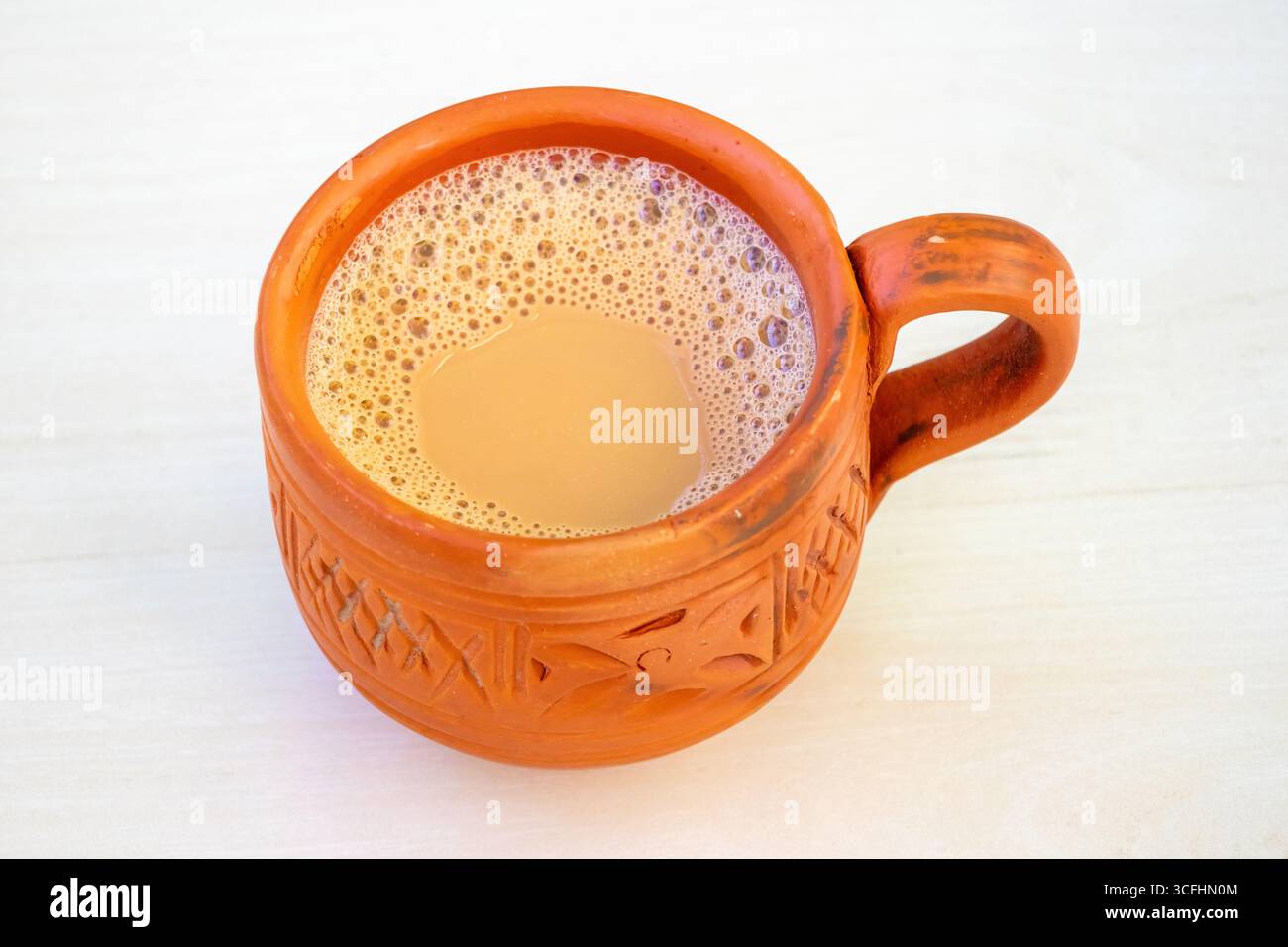 Una tazza di tè al latte caldo o di dudh cha in una tradizionale tazza di argilla posta su una superficie di legno chiaro. Gustosi doodh chai in una tazza di terracotta. E' un estremo Foto Stock