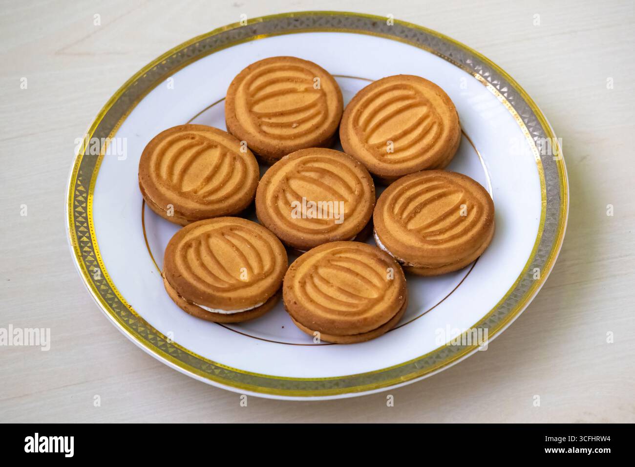 Deliziosi biscotti di frumento ripieni di panna da latte serviti su un piatto bianco su sfondo di legno. Foto Stock