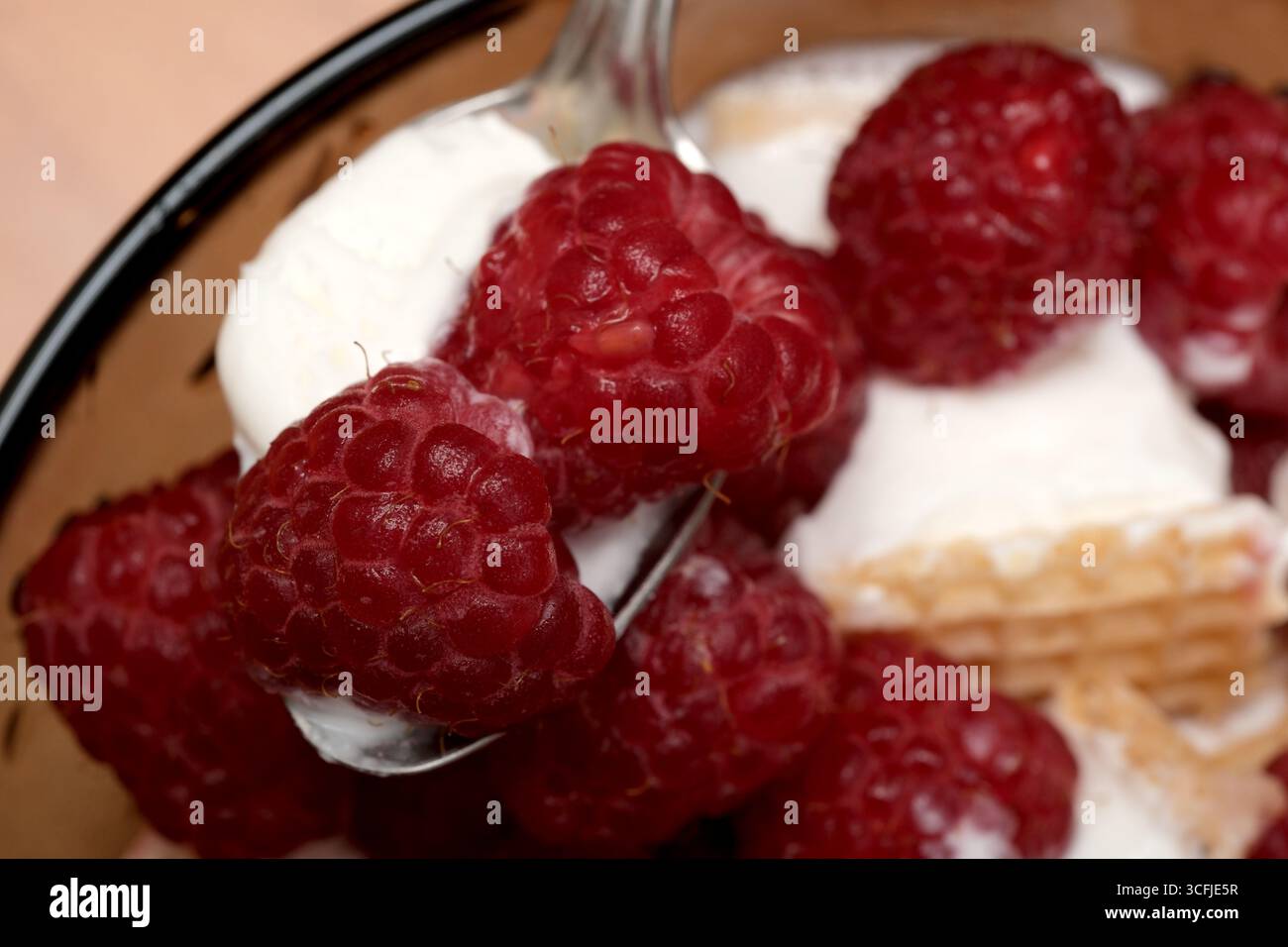 Un cucchiaio di dessert cremoso adornato da vibranti e succosi lamponi delizia i sensi. Foto Stock
