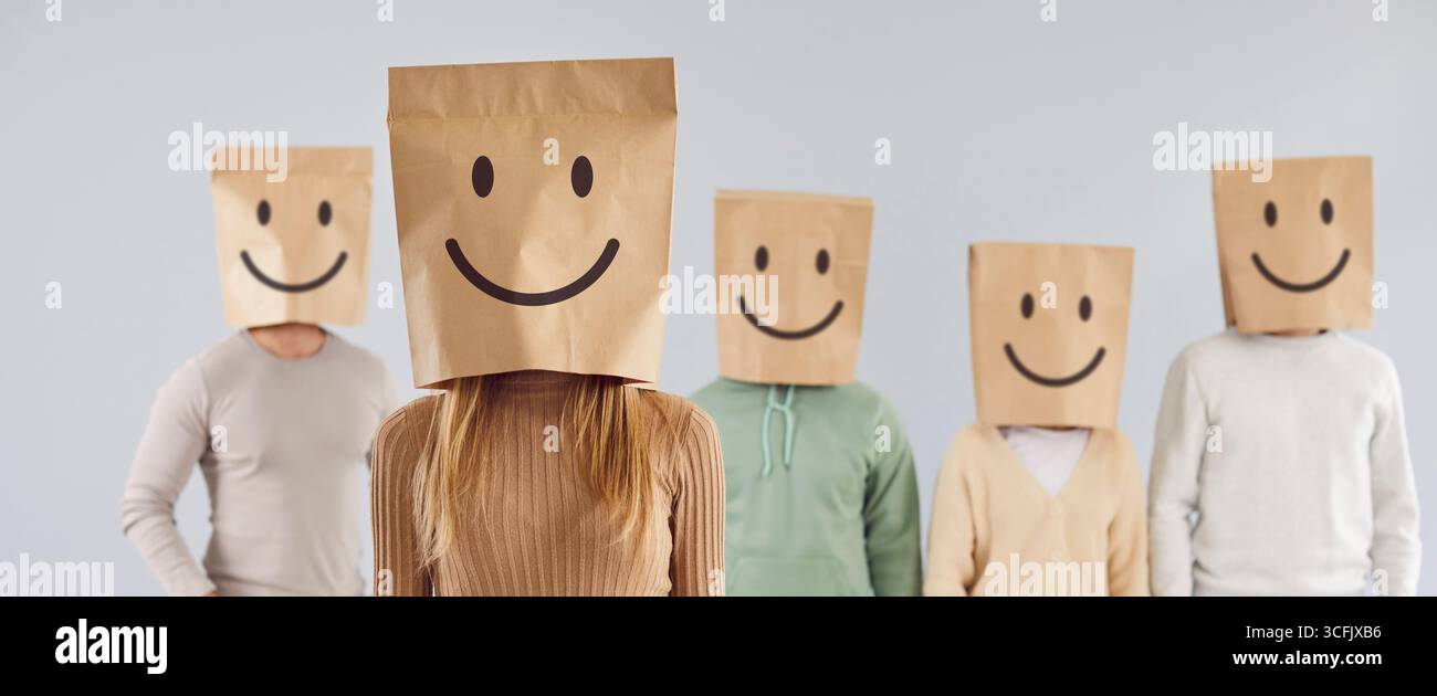 Un gruppo di persone non identificate trasporta sacchetti di carta con emoticon sorridenti dipinte sulle teste. Foto Stock