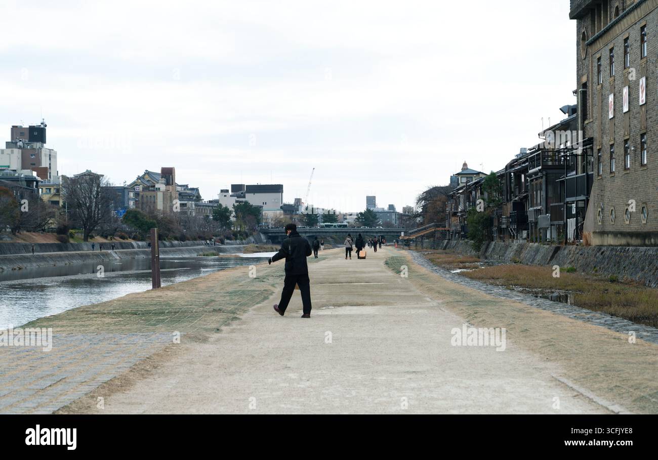 I pedoni passeggiano lungo la passeggiata sul fiume Kamo a Kyoto in una nuvolosa giornata invernale Foto Stock
