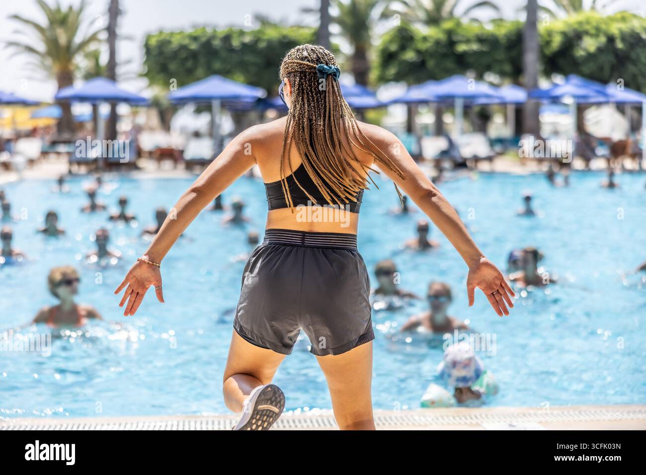 Una giovane donna animatrice sportiva sta facendo aerobica in acqua per le persone nella piscina di un hotel resort. Foto Stock
