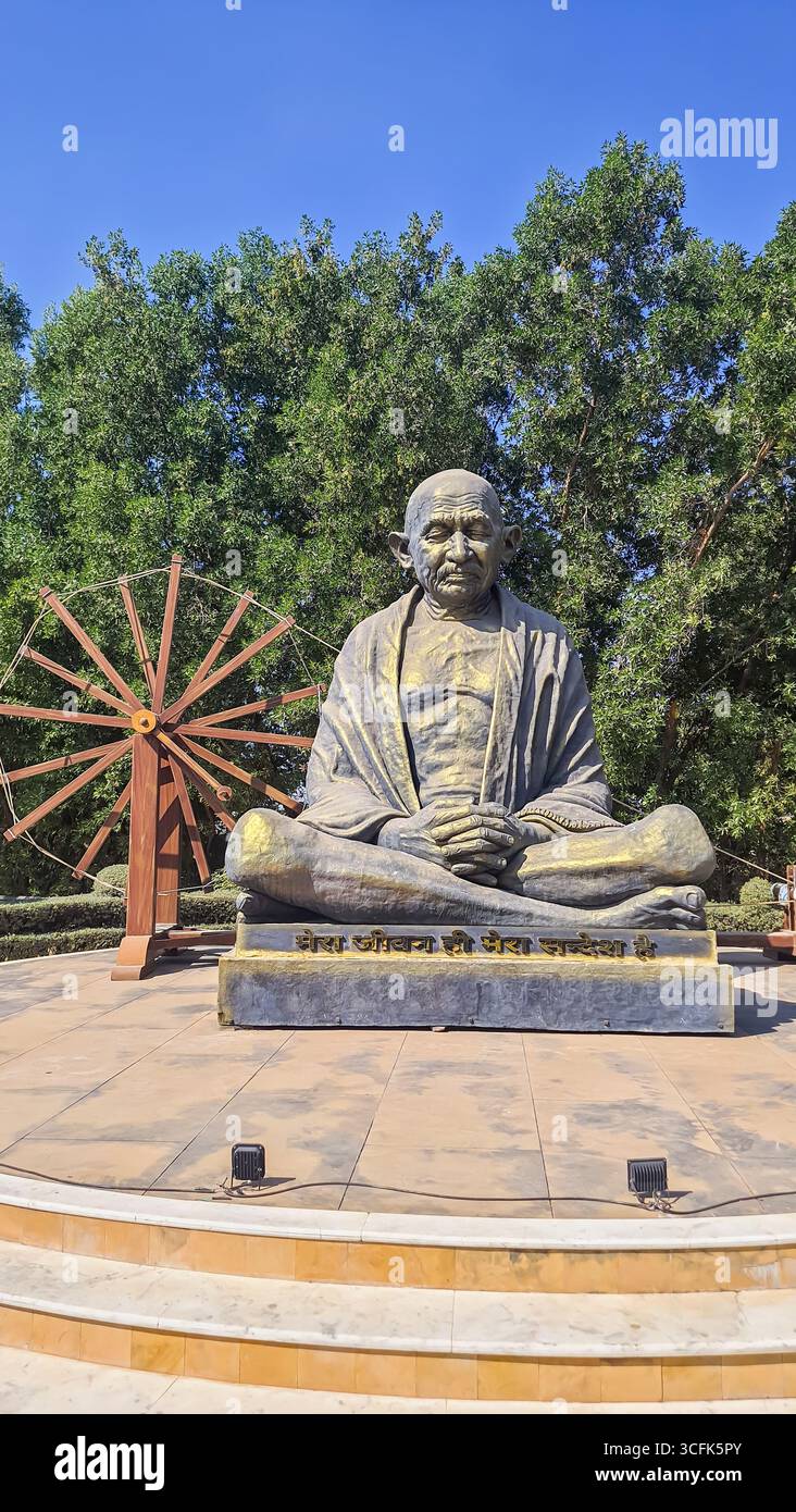 scultura isolata in pietra mahatma gandhi con charkha alla luce del giorno Foto Stock