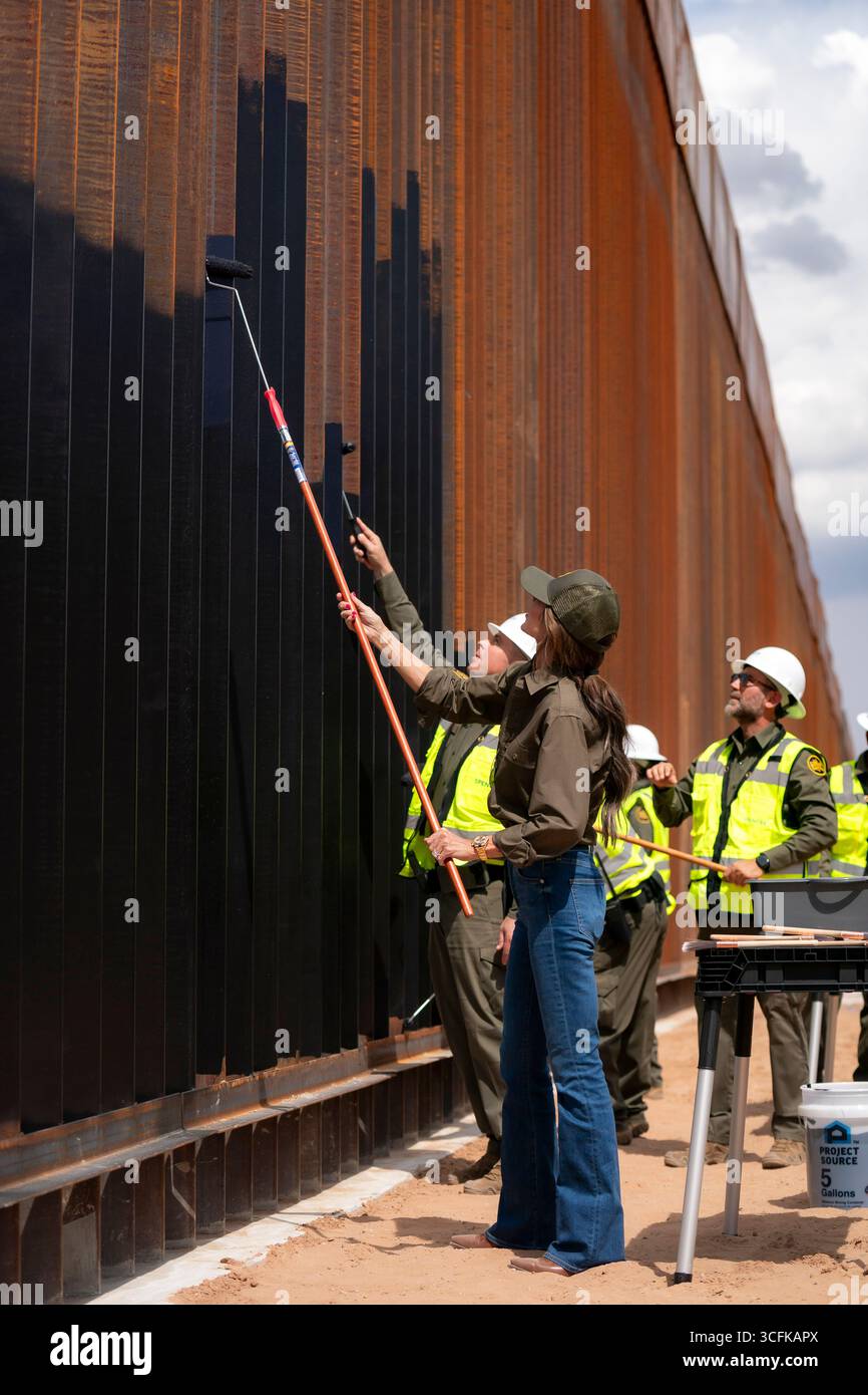 Il segretario del Dipartimento per la sicurezza interna (DHS) Kristi Noem ha viaggiato su un jet militare e poi su un elicottero fino al muro del confine meridionale degli Stati Uniti, dove ha in mano una foto - sotto la direzione del presidente Donald Trump - per dipingere il muro d'acciaio del confine nero a Santa Teresa, New Mexico. Noem è stato assistito da membri in uniforme degli agenti della dogana e della protezione delle frontiere degli Stati Uniti. La vernice nera doveva raccogliere l’energia del sole per rendere l’acciaio del muro più caldo al tatto – quindi più difficile per i clandestini scalare. La vernice, tuttavia, veniva applicata solo sul lato statunitense del muro di confine. Foto Stock