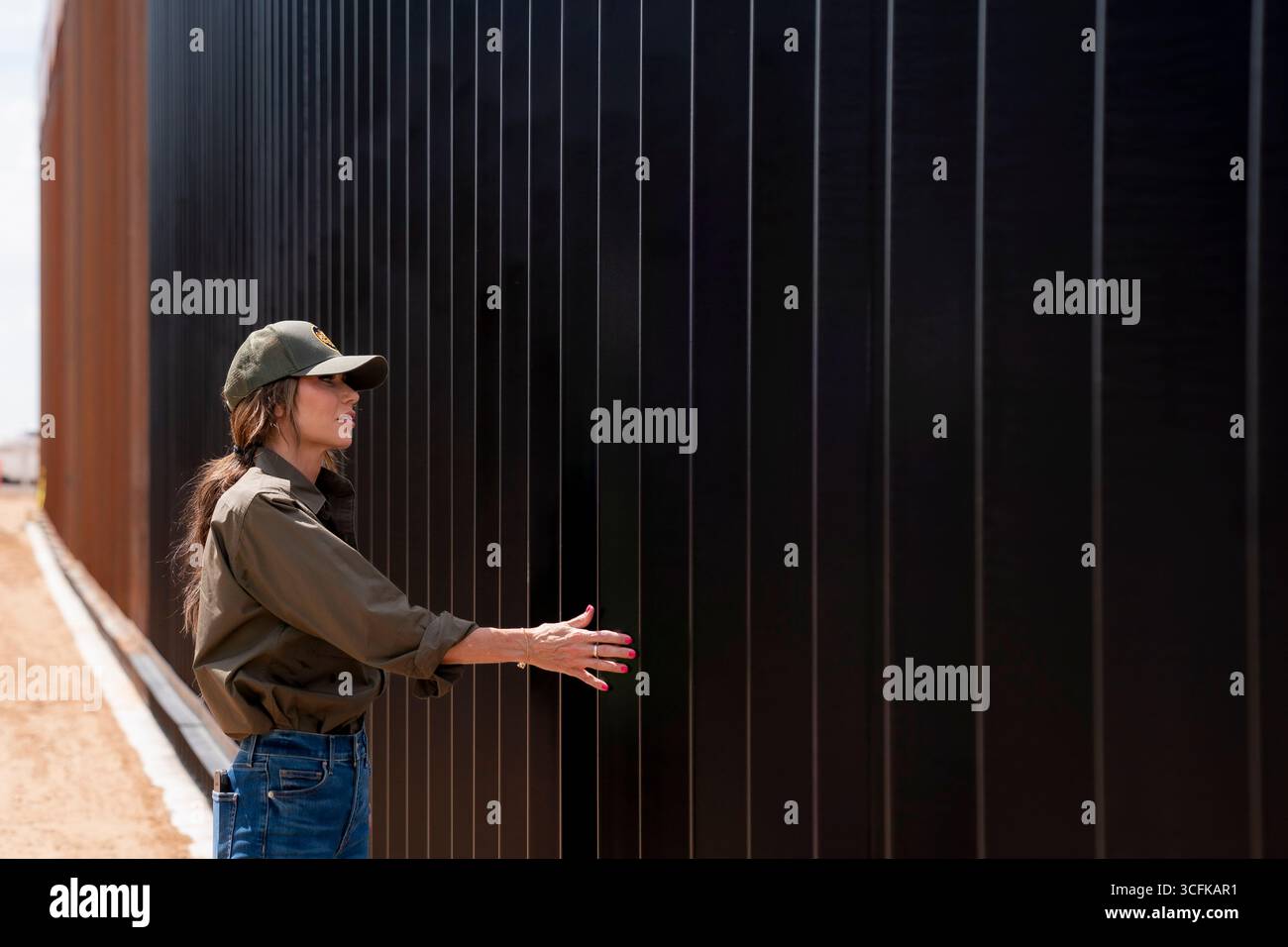 Il segretario del Dipartimento per la sicurezza interna (DHS) Kristi Noem ha viaggiato su un jet militare e poi su un elicottero fino al muro del confine meridionale degli Stati Uniti, dove ha in mano una foto - sotto la direzione del presidente Donald Trump - per dipingere il muro d'acciaio del confine nero a Santa Teresa, New Mexico. Noem è stato assistito da membri in uniforme degli agenti della dogana e della protezione delle frontiere degli Stati Uniti. La vernice nera doveva raccogliere l’energia del sole per rendere l’acciaio del muro più caldo al tatto – quindi più difficile per i clandestini scalare. La vernice, tuttavia, veniva applicata solo sul lato statunitense del muro di confine. Foto Stock