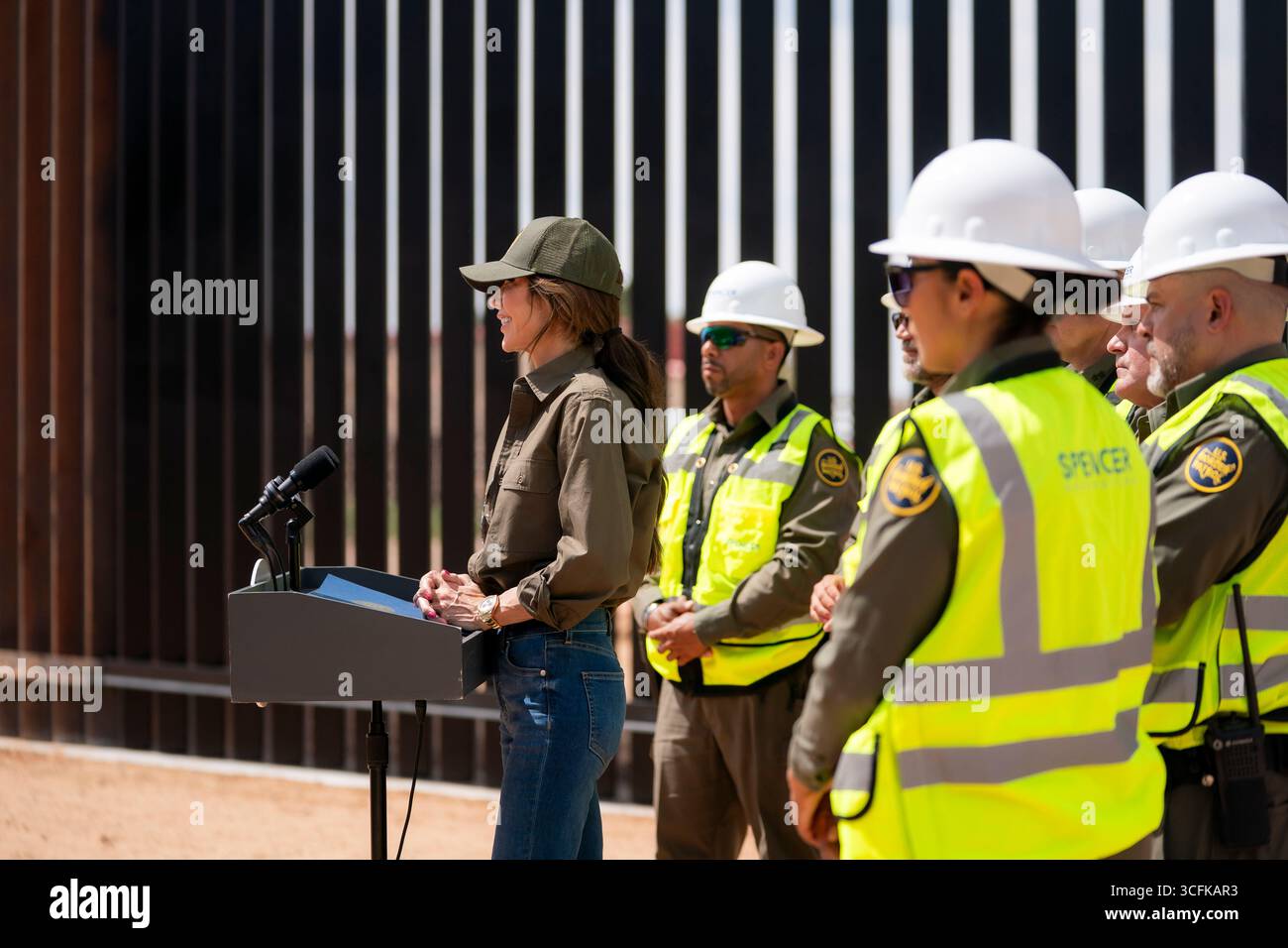 Il segretario del Dipartimento per la sicurezza interna (DHS) Kristi Noem ha viaggiato su un jet militare e poi su un elicottero fino al muro del confine meridionale degli Stati Uniti, dove ha in mano una foto - sotto la direzione del presidente Donald Trump - per dipingere il muro d'acciaio del confine nero a Santa Teresa, New Mexico. Noem è stato assistito da membri in uniforme degli agenti della dogana e della protezione delle frontiere degli Stati Uniti. La vernice nera doveva raccogliere l’energia del sole per rendere l’acciaio del muro più caldo al tatto – quindi più difficile per i clandestini scalare. La vernice, tuttavia, veniva applicata solo sul lato statunitense del muro di confine. Foto Stock