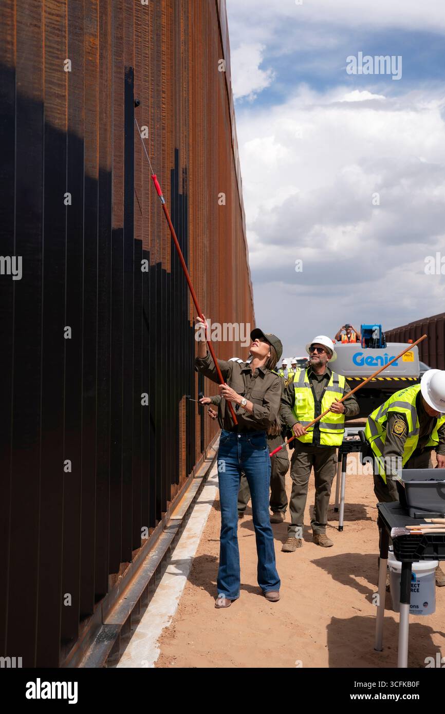 Il segretario del Dipartimento per la sicurezza interna (DHS) Kristi Noem ha viaggiato su un jet militare e poi su un elicottero fino al muro del confine meridionale degli Stati Uniti, dove ha in mano una foto - sotto la direzione del presidente Donald Trump - per dipingere il muro d'acciaio del confine nero a Santa Teresa, New Mexico. Noem è stato assistito da membri in uniforme degli agenti della dogana e della protezione delle frontiere degli Stati Uniti. La vernice nera doveva raccogliere l’energia del sole per rendere l’acciaio del muro più caldo al tatto – quindi più difficile per i clandestini scalare. La vernice, tuttavia, veniva applicata solo sul lato statunitense del muro di confine. Foto Stock