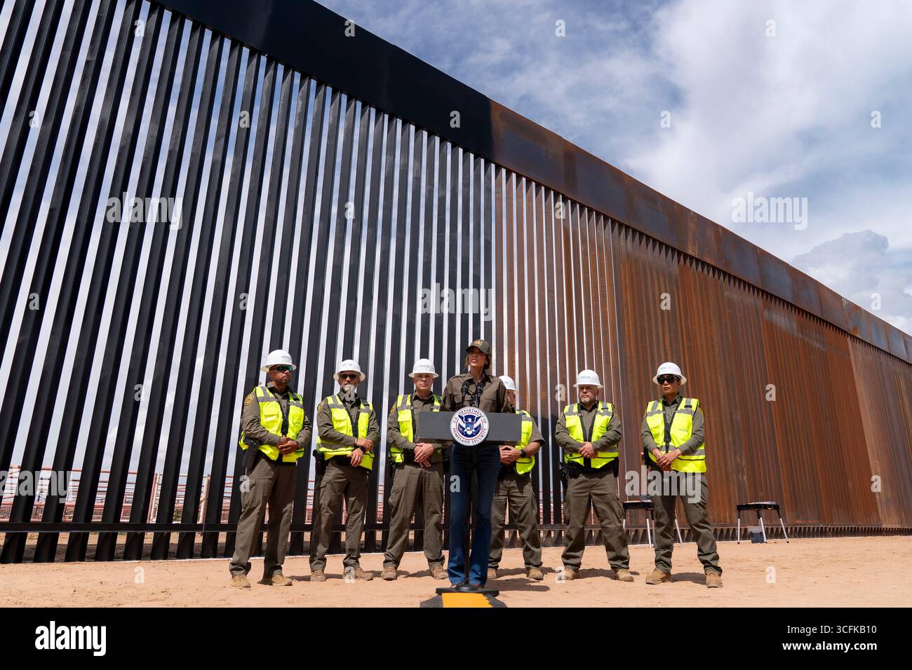 Il segretario del Dipartimento per la sicurezza interna (DHS) Kristi Noem ha viaggiato su un jet militare e poi su un elicottero fino al muro del confine meridionale degli Stati Uniti, dove ha in mano una foto - sotto la direzione del presidente Donald Trump - per dipingere il muro d'acciaio del confine nero a Santa Teresa, New Mexico. Noem è stato assistito da membri in uniforme degli agenti della dogana e della protezione delle frontiere degli Stati Uniti. La vernice nera doveva raccogliere l’energia del sole per rendere l’acciaio del muro più caldo al tatto – quindi più difficile per i clandestini scalare. La vernice, tuttavia, veniva applicata solo sul lato statunitense del muro di confine. Foto Stock