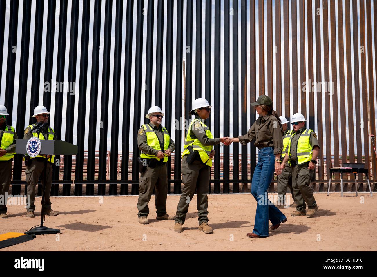 Il segretario del Dipartimento per la sicurezza interna (DHS) Kristi Noem ha viaggiato su un jet militare e poi su un elicottero fino al muro del confine meridionale degli Stati Uniti, dove ha in mano una foto - sotto la direzione del presidente Donald Trump - per dipingere il muro d'acciaio del confine nero a Santa Teresa, New Mexico. Noem è stato assistito da membri in uniforme degli agenti della dogana e della protezione delle frontiere degli Stati Uniti. La vernice nera doveva raccogliere l’energia del sole per rendere l’acciaio del muro più caldo al tatto – quindi più difficile per i clandestini scalare. La vernice, tuttavia, veniva applicata solo sul lato statunitense del muro di confine. Foto Stock