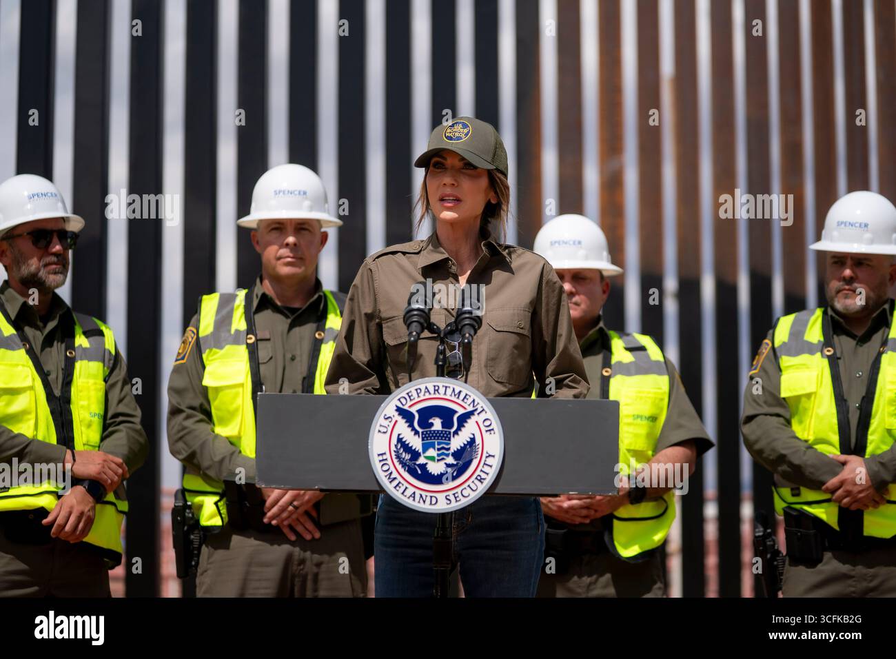 Il segretario del Dipartimento per la sicurezza interna (DHS) Kristi Noem ha viaggiato su un jet militare e poi su un elicottero fino al muro del confine meridionale degli Stati Uniti, dove ha in mano una foto - sotto la direzione del presidente Donald Trump - per dipingere il muro d'acciaio del confine nero a Santa Teresa, New Mexico. Noem è stato assistito da membri in uniforme degli agenti della dogana e della protezione delle frontiere degli Stati Uniti. La vernice nera doveva raccogliere l’energia del sole per rendere l’acciaio del muro più caldo al tatto – quindi più difficile per i clandestini scalare. La vernice, tuttavia, veniva applicata solo sul lato statunitense del muro di confine. Foto Stock