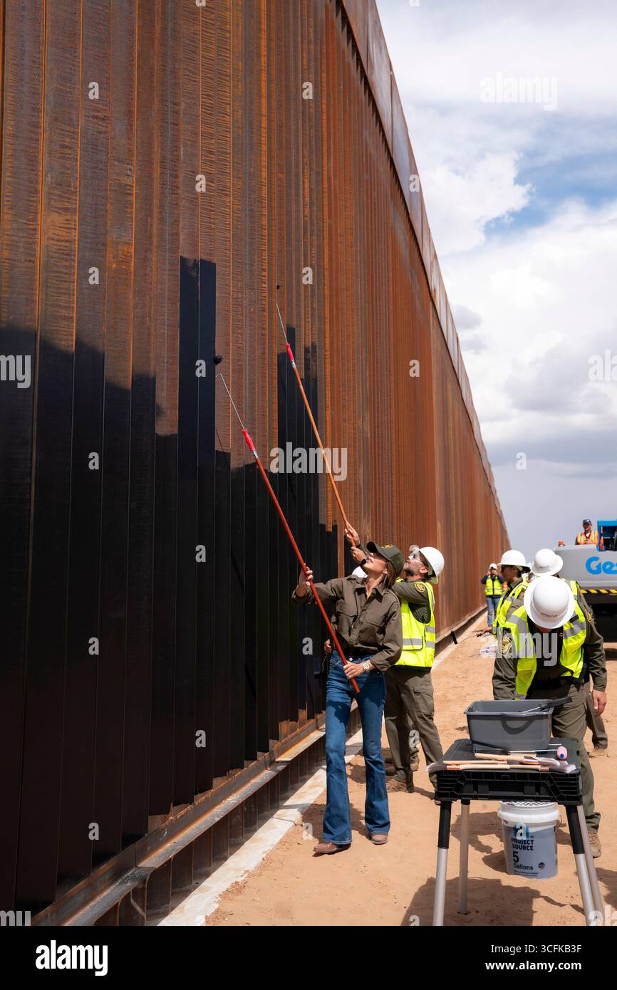 Il segretario del Dipartimento per la sicurezza interna (DHS) Kristi Noem ha viaggiato su un jet militare e poi su un elicottero fino al muro del confine meridionale degli Stati Uniti, dove ha in mano una foto - sotto la direzione del presidente Donald Trump - per dipingere il muro d'acciaio del confine nero a Santa Teresa, New Mexico. Noem è stato assistito da membri in uniforme degli agenti della dogana e della protezione delle frontiere degli Stati Uniti. La vernice nera doveva raccogliere l’energia del sole per rendere l’acciaio del muro più caldo al tatto – quindi più difficile per i clandestini scalare. La vernice, tuttavia, veniva applicata solo sul lato statunitense del muro di confine. Foto Stock