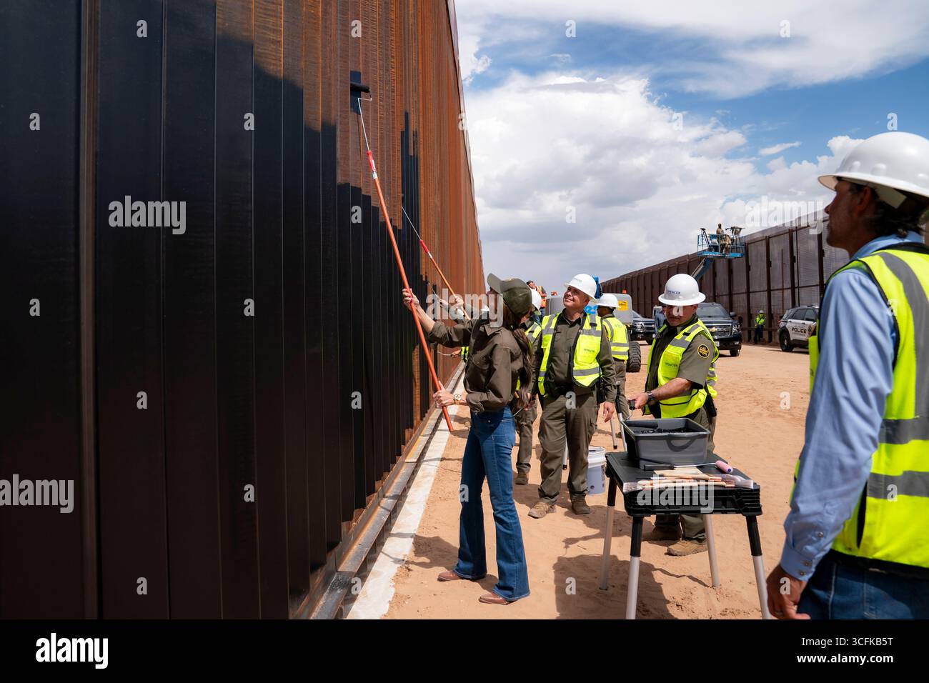 Il segretario del Dipartimento per la sicurezza interna (DHS) Kristi Noem ha viaggiato su un jet militare e poi su un elicottero fino al muro del confine meridionale degli Stati Uniti, dove ha in mano una foto - sotto la direzione del presidente Donald Trump - per dipingere il muro d'acciaio del confine nero a Santa Teresa, New Mexico. Noem è stato assistito da membri in uniforme degli agenti della dogana e della protezione delle frontiere degli Stati Uniti. La vernice nera doveva raccogliere l’energia del sole per rendere l’acciaio del muro più caldo al tatto – quindi più difficile per i clandestini scalare. La vernice, tuttavia, veniva applicata solo sul lato statunitense del muro di confine. Foto Stock