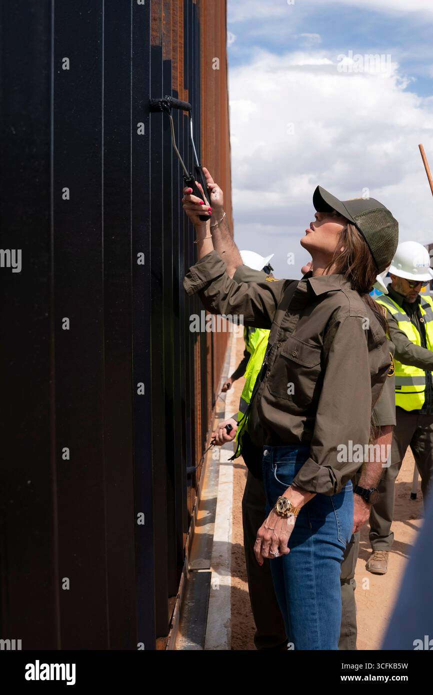 Il segretario del Dipartimento per la sicurezza interna (DHS) Kristi Noem ha viaggiato su un jet militare e poi su un elicottero fino al muro del confine meridionale degli Stati Uniti, dove ha in mano una foto - sotto la direzione del presidente Donald Trump - per dipingere il muro d'acciaio del confine nero a Santa Teresa, New Mexico. Noem è stato assistito da membri in uniforme degli agenti della dogana e della protezione delle frontiere degli Stati Uniti. La vernice nera doveva raccogliere l’energia del sole per rendere l’acciaio del muro più caldo al tatto – quindi più difficile per i clandestini scalare. La vernice, tuttavia, veniva applicata solo sul lato statunitense del muro di confine. Foto Stock