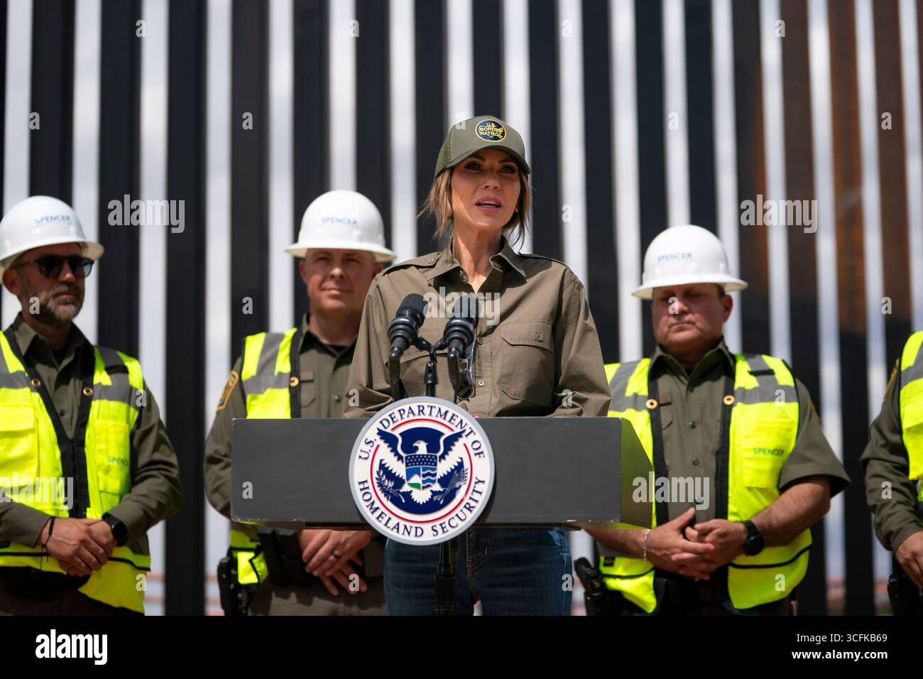 Il segretario del Dipartimento per la sicurezza interna (DHS) Kristi Noem ha viaggiato su un jet militare e poi su un elicottero fino al muro del confine meridionale degli Stati Uniti, dove ha in mano una foto - sotto la direzione del presidente Donald Trump - per dipingere il muro d'acciaio del confine nero a Santa Teresa, New Mexico. Noem è stato assistito da membri in uniforme degli agenti della dogana e della protezione delle frontiere degli Stati Uniti. La vernice nera doveva raccogliere l’energia del sole per rendere l’acciaio del muro più caldo al tatto – quindi più difficile per i clandestini scalare. La vernice, tuttavia, veniva applicata solo sul lato statunitense del muro di confine. Foto Stock