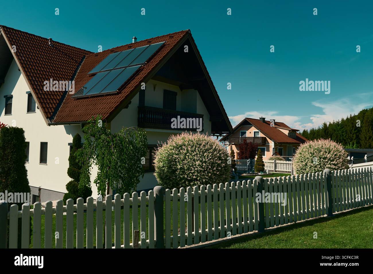 Casa con tetto rosso, pannelli solari e giardino perfettamente curato con arbusti in fiore rosa-bianco sferici e alberi topiari. Foto Stock
