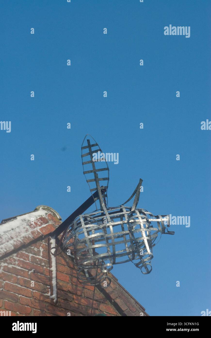 Una scultura creativa in metallo a forma di maiale è installata sul tetto di un edificio in mattoni, che mostra espressione artistica contro un cielo blu brillante. Foto Stock