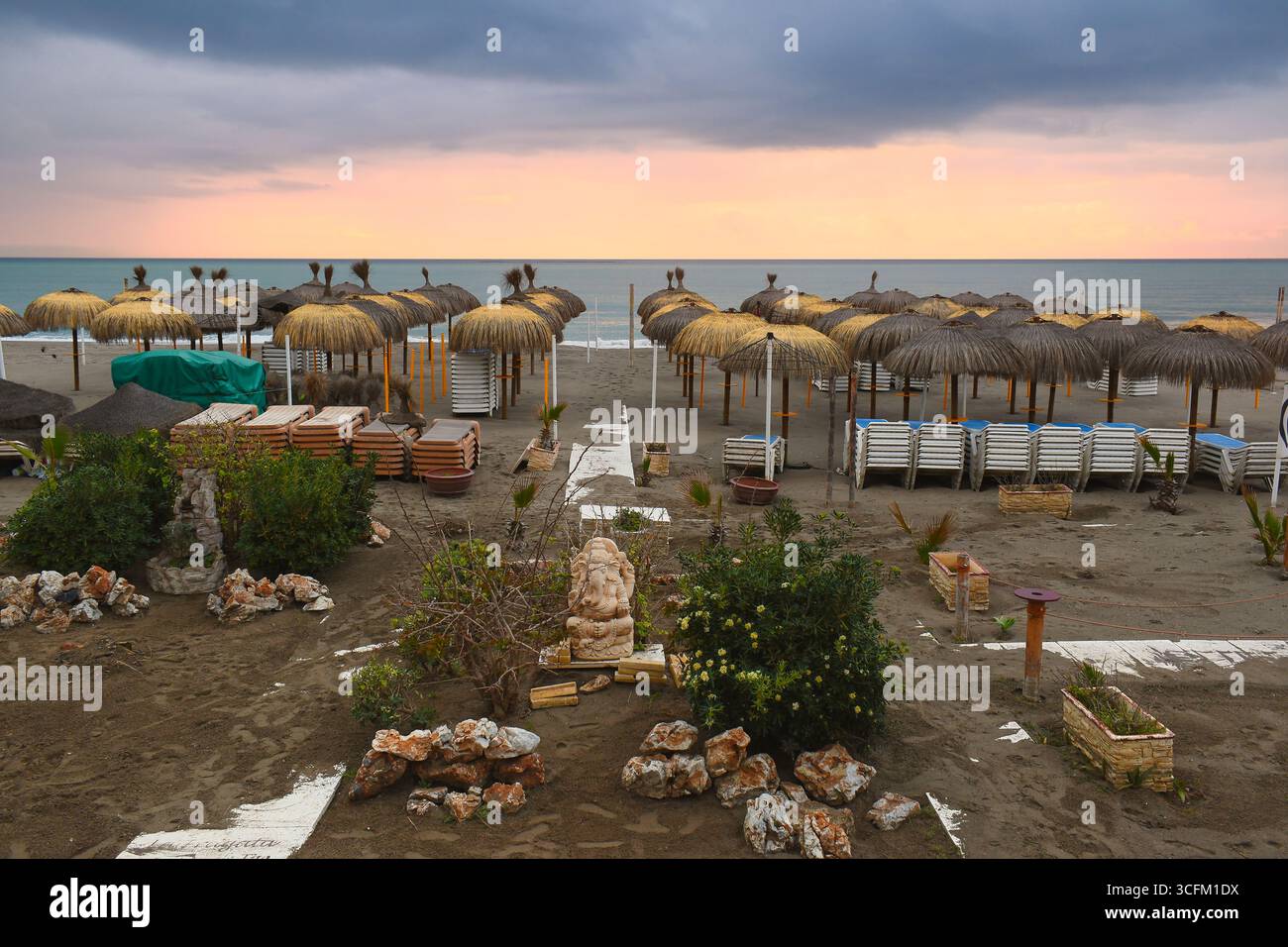 Vista al tramonto della spiaggia vuota con ombrelloni di paglia a Benalmadena Malaga Spagna costa mediterranea, destinazione di viaggio per le vacanze Foto Stock