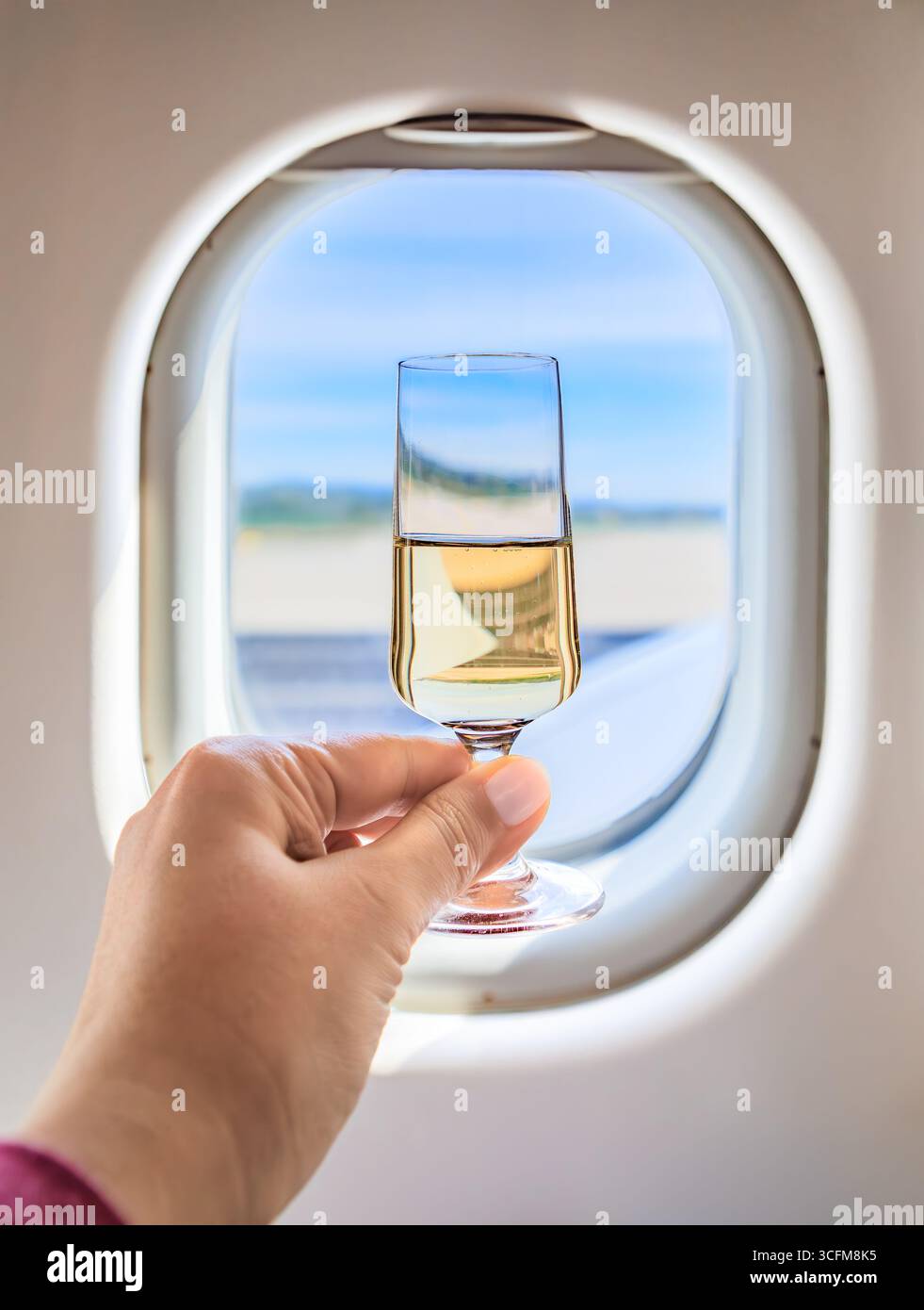 Una mano solleva un bicchiere di champagne in un brindisi, vista della pista e del cielo aperto dalla finestra dell'aereo, esperienza di viaggio di lusso in business class Foto Stock