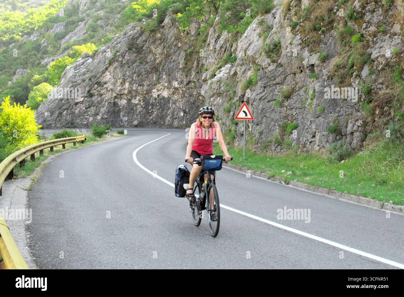 Donna sorridente in bicicletta su una strada di montagna della Baia di Cattaro in Montenegro Foto Stock