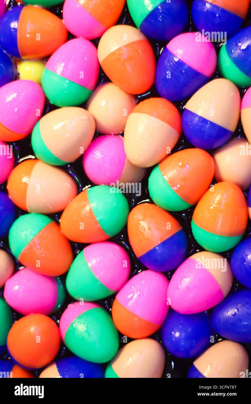 Sfondo verticale astratto con uova di plastica lucide a metà colore sull'acqua. Riflessi giocosi in colori vivaci e vivaci. Foto Stock
