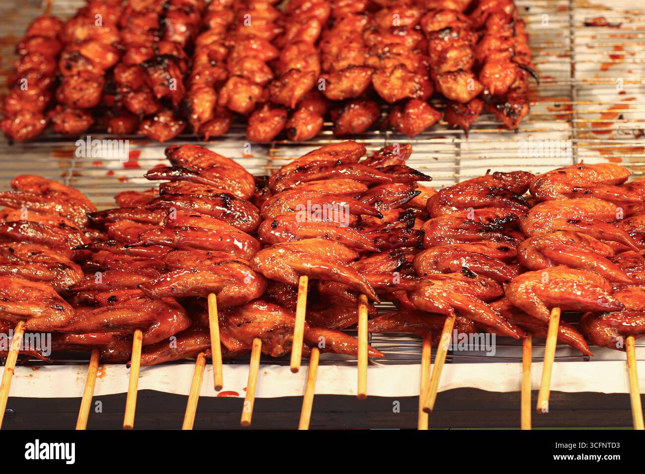 Ali di pollo tailandese grigliate sugli spiedini, glassate con salsa dolce rossa lucida, evidenziano il cibo di strada asiatico e la cultura culinaria del turismo. Foto Stock