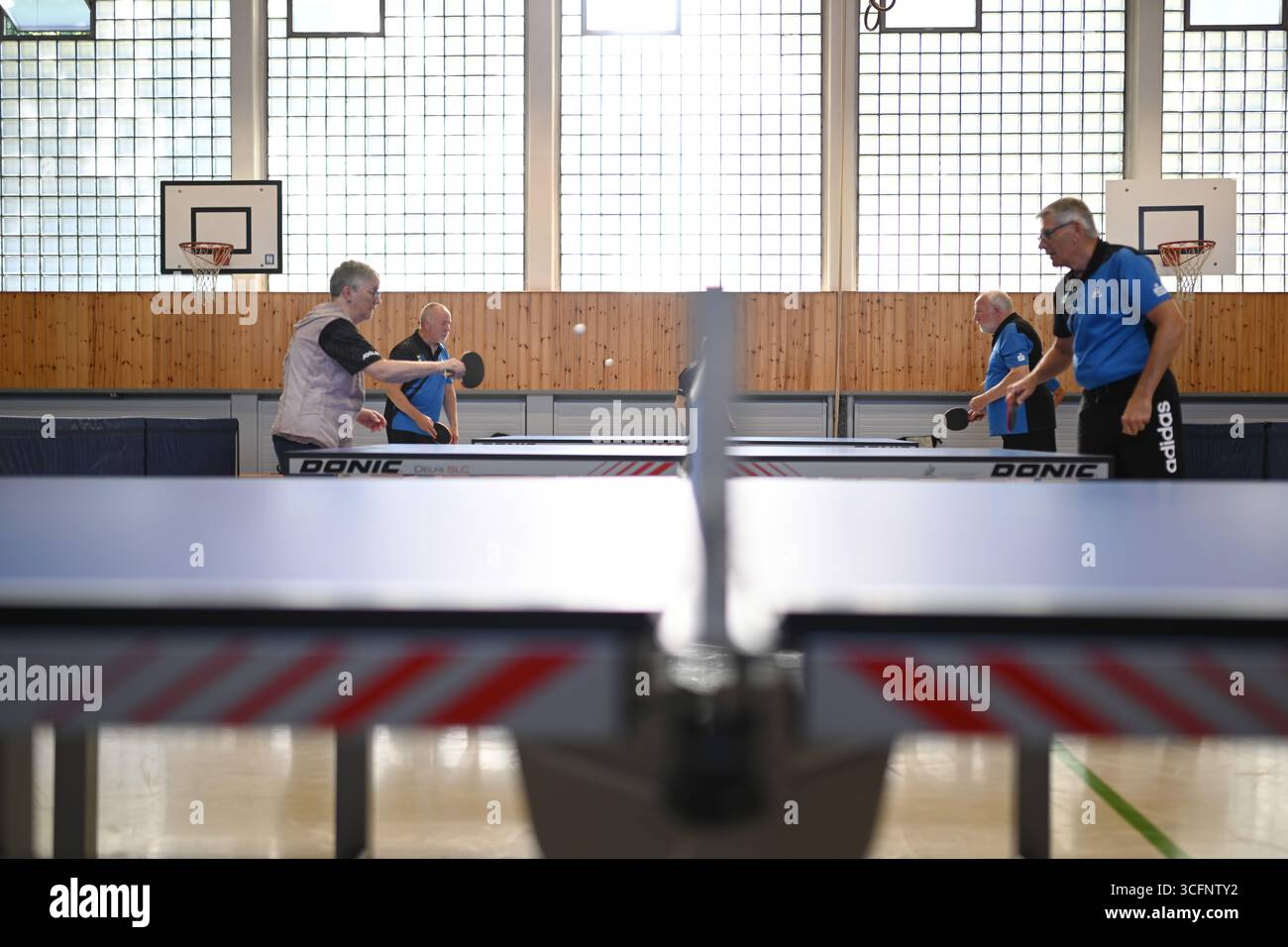 PRODUZIONE - 24 agosto 2025, bassa Sassonia, Warsingsfehn: I membri si allenano in piccoli gruppi su diversi tavoli. I membri del Ping-Pong Parkinson (PPP) a Warsingsfehn si incontrano regolarmente in palestra per giocare a ping-pong insieme. Questo allenamento non è solo sport: Aiuta le persone colpite a rimanere attive e a mantenere il proprio corpo mobile. Il Parkinson limita sempre di più la mobilità e il coordinamento, ma il gioco frenetico al tavolo da ping-pong promuove le capacità motorie, la reazione e la concentrazione. Il PPP rappresenta quindi non solo un equilibrio sportivo per i membri, ma anche una parte importante della concessionaria Foto Stock