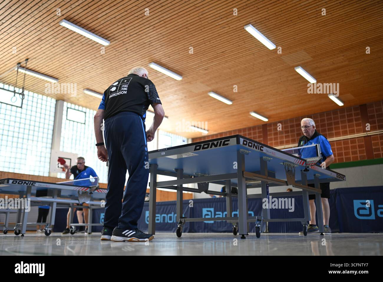 PRODUZIONE - 24 agosto 2025, bassa Sassonia, Warsingsfehn: I membri si allenano in piccoli gruppi su diversi tavoli. I membri del Ping-Pong Parkinson (PPP) a Warsingsfehn si incontrano regolarmente in palestra per giocare a ping-pong insieme. Questo allenamento non è solo sport: Aiuta le persone colpite a rimanere attive e a mantenere il proprio corpo mobile. Il Parkinson limita sempre di più la mobilità e il coordinamento, ma il gioco frenetico al tavolo da ping-pong promuove le capacità motorie, la reazione e la concentrazione. Il PPP rappresenta quindi non solo un equilibrio sportivo per i membri, ma anche una parte importante della concessionaria Foto Stock