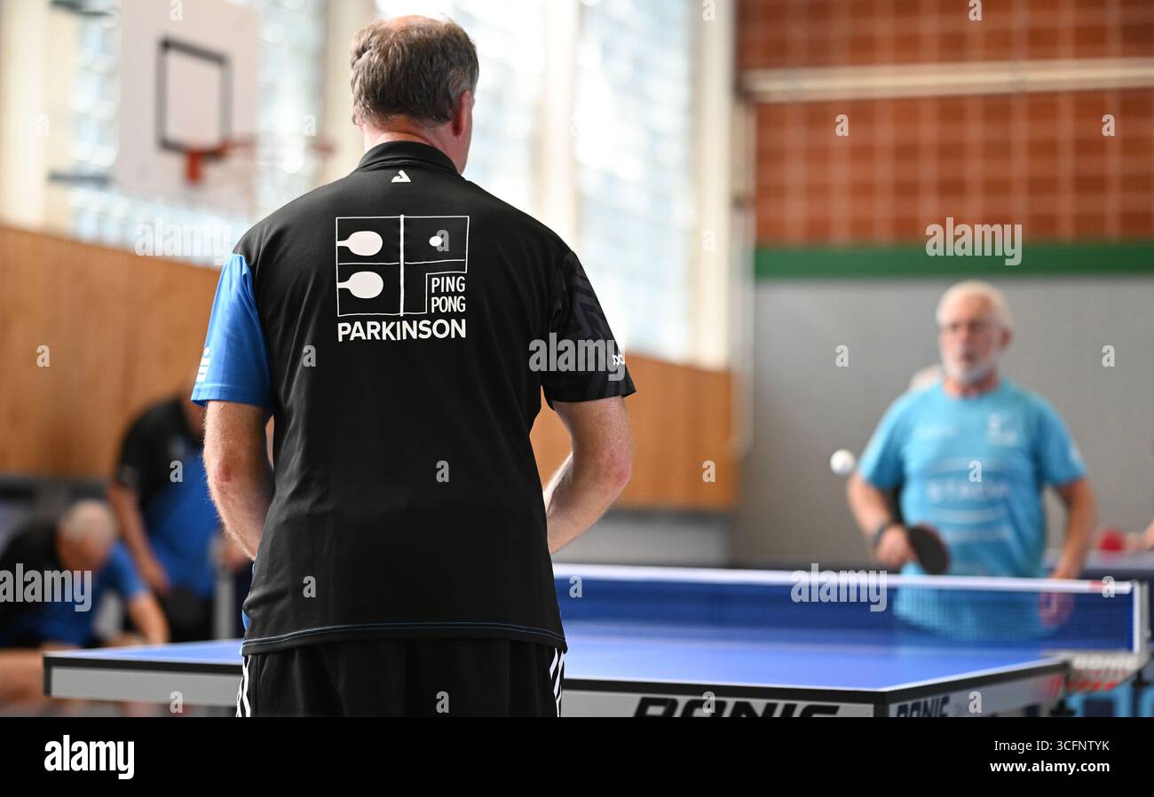 PRODUZIONE - 24 agosto 2025, bassa Sassonia, Warsingsfehn: I membri si allenano in piccoli gruppi su diversi tavoli. I membri del Ping-Pong Parkinson (PPP) a Warsingsfehn si incontrano regolarmente in palestra per giocare a ping-pong insieme. Questo allenamento non è solo sport: Aiuta le persone colpite a rimanere attive e a mantenere il proprio corpo mobile. Il Parkinson limita sempre di più la mobilità e il coordinamento, ma il gioco frenetico al tavolo da ping-pong promuove le capacità motorie, la reazione e la concentrazione. Il PPP rappresenta quindi non solo un equilibrio sportivo per i membri, ma anche una parte importante della concessionaria Foto Stock