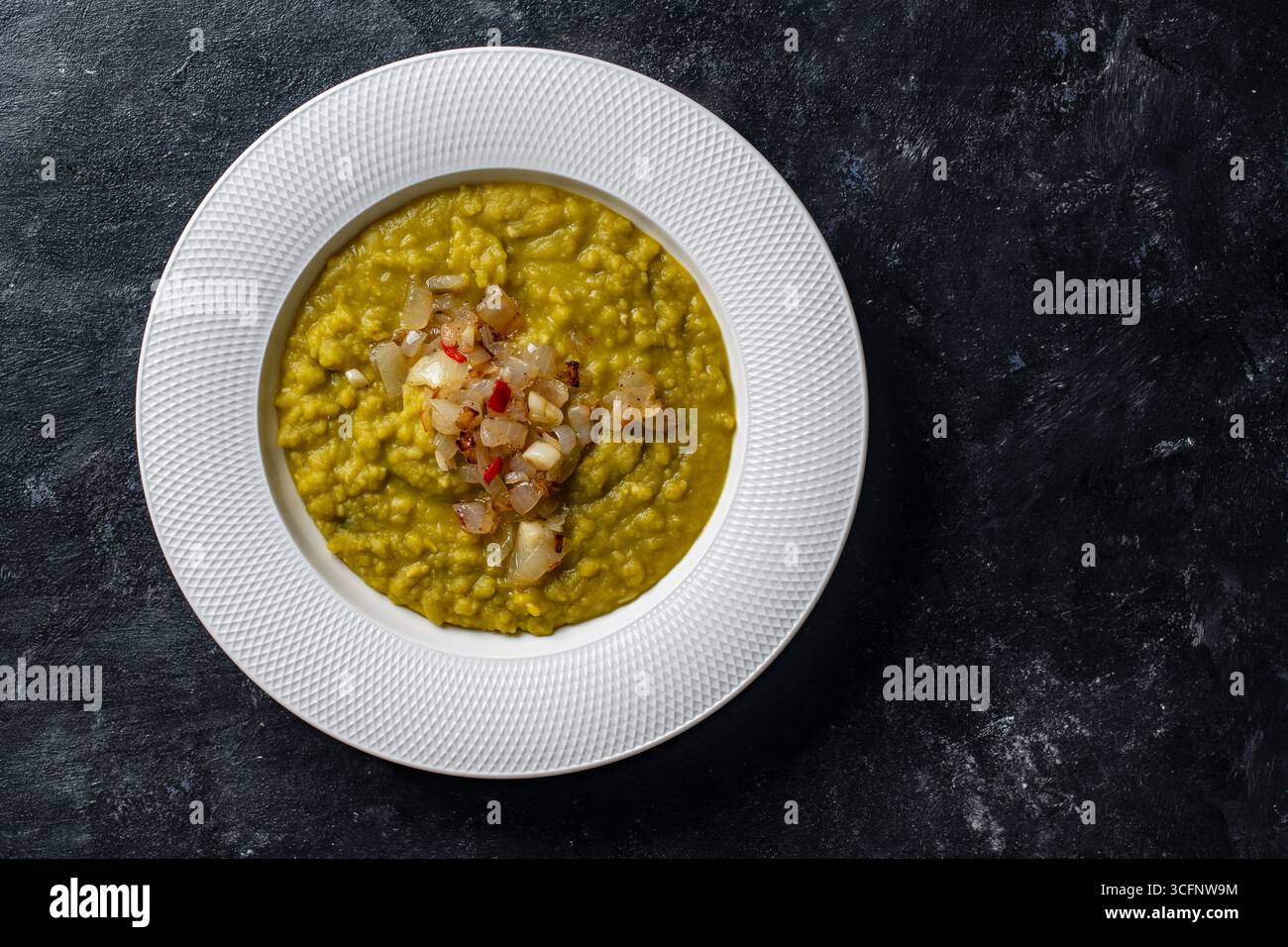 Purea di piselli verdi con cipolle fritte in un piatto bianco con spezie sul tavolo, primo piano, vista dall'alto. Cibo sano, deliziosa zuppa di piselli secchi Foto Stock