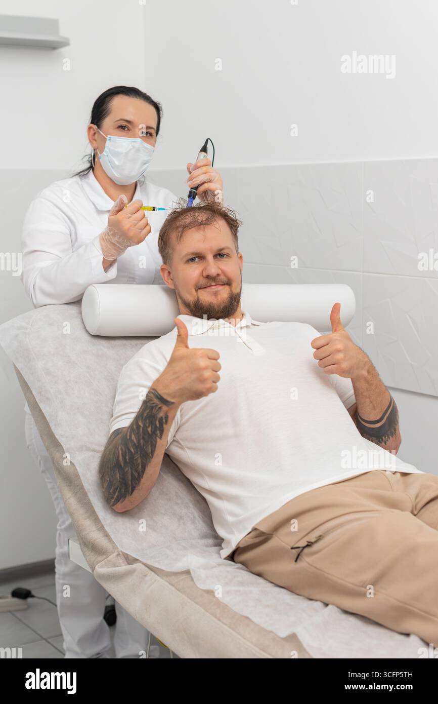 Alopecia. Perdita di capelli migliorare il trattamento della crescita dermapen microneedling vitamine esosomi iniezioni di siringhe di plasma. Mesoterapia frazionata con procedura alla testa di cosmetologo. Uomo felice che mostra i pollici in alto come. Foto Stock