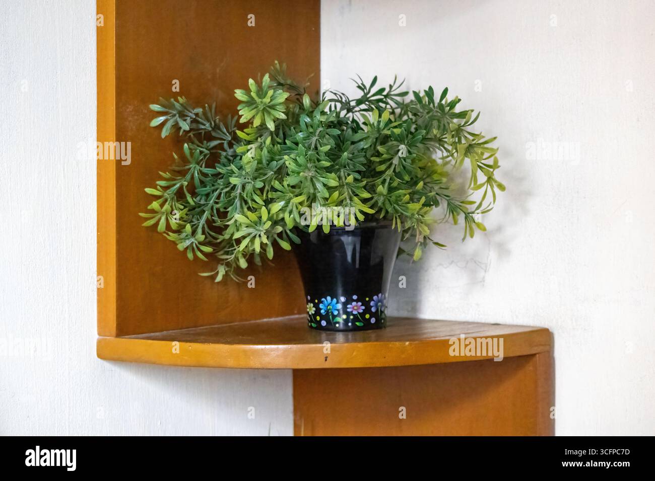 Primo piano di un ripiano angolare in legno con una pianta artificiale in vaso, scaffale a parete per l'arredamento della casa. Foto Stock